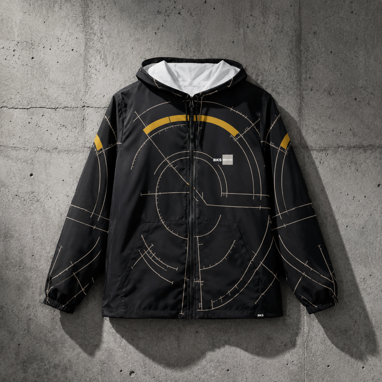 BKS Hours Arc Windbreaker — front hero on brutalist concrete wall, arc construction lines in silver and gold